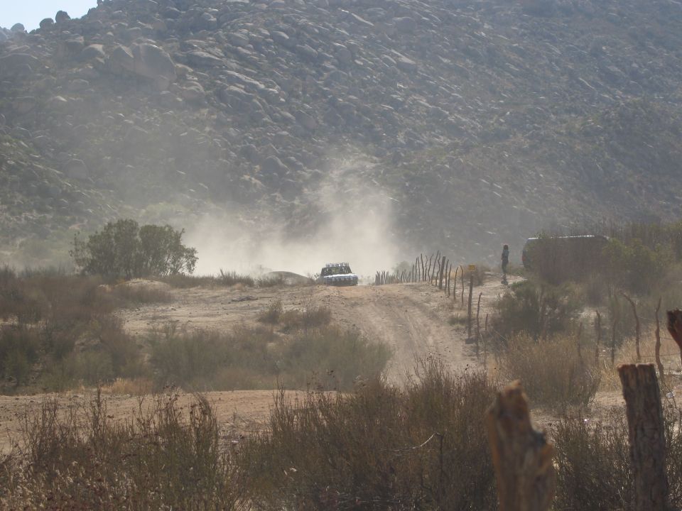 Dusty off-road vehicle kicking up dust on a dirt track with a rocky hill in the background