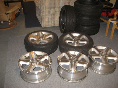 1997 Acura TL - A collection of alloy wheels and tires are displayed on a carpeted floor indoors.