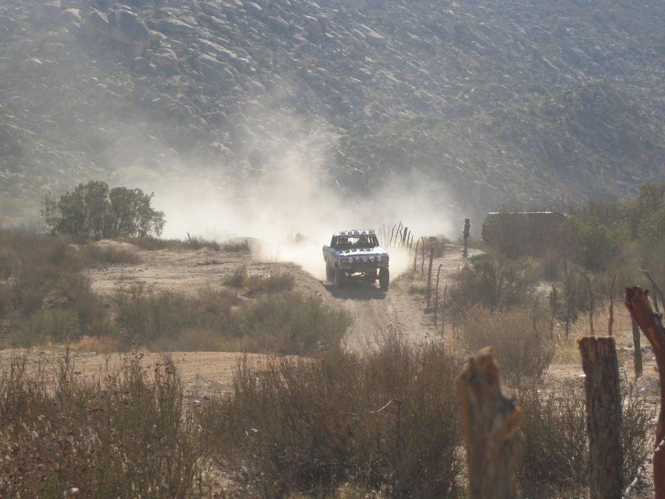 Off-road truck kicking up dust on a dirt track with hills in the background