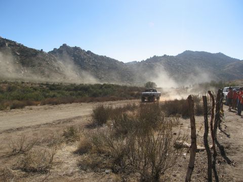 1986 Ford Bronco - A race truck navigates a dusty course during the Baja 1000 2009 event, with spectators watching from the side.