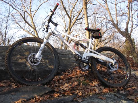 1981 Garelli Rally Sport - A white mountain bike is parked on a large rock outdoors, surrounded by trees and fallen leaves.