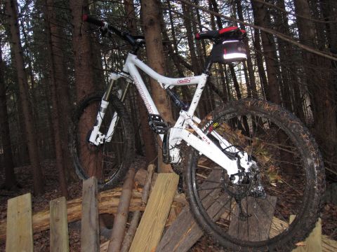 1981 Garelli Rally Sport - A white Cannondale mountain bike is parked in a wooded area, resting on a makeshift wooden platform.