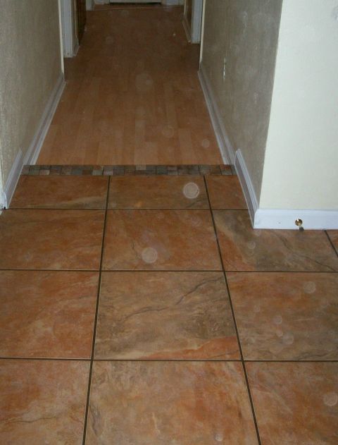 1993 Ford Bronco - Interior home flooring shot showing large rust-toned tile in a foyer meeting laminate wood flooring in a hallway, joined by a mosaic accent…