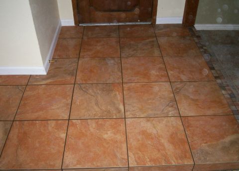1993 Ford Bronco - Interior foyer floor tiled in large rust and tan stone-look ceramic tiles with thin dark grout lines, running up to the threshold of a dark…
