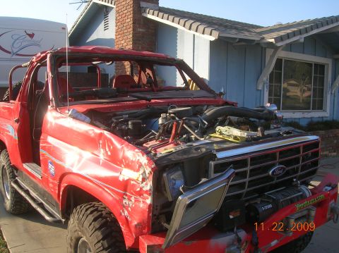 1985 Ford Bronco - This heavily damaged red Ford Bronco shows significant front-end collision impact and an open hood revealing the engine.