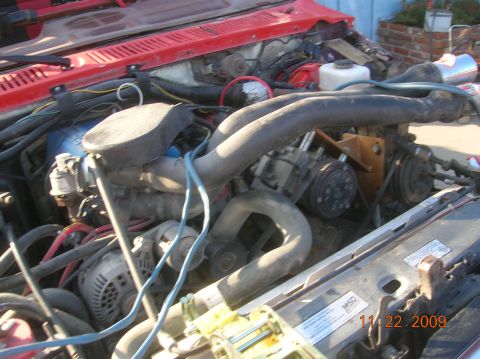 1985 Ford Bronco - The engine bay of a red 1985 Ford Bronco, its V8 engine and various mechanical parts.