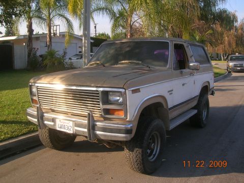 1985 Ford Bronco - This two-tone Ford Bronco is parked on a residential street with palm trees in the background.