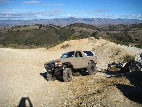 1989 Ford Bronco - A modified Ford Bronco navigates a , hilly terrain under a clear blue sky.