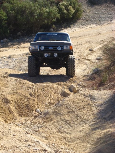 1989 Ford Bronco - A modified Ford Bronco navigates a rough, dusty trail in a hilly, arid landscape.
