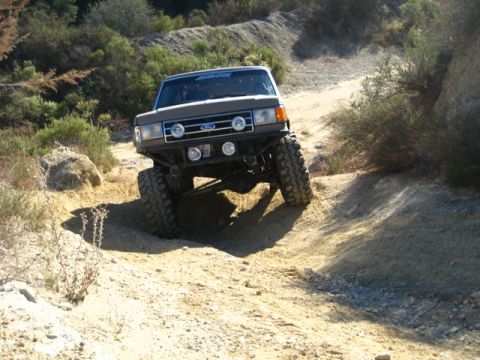 1989 Ford Bronco - Ford Bronco navigating a steep, dusty off-road trail with significant suspension articulation.