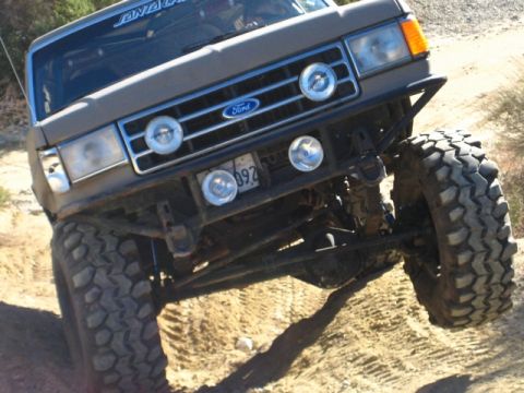 1989 Ford Bronco - This modified Ford Bronco is navigating a sandy, off-road terrain with its large, aggressive tires.