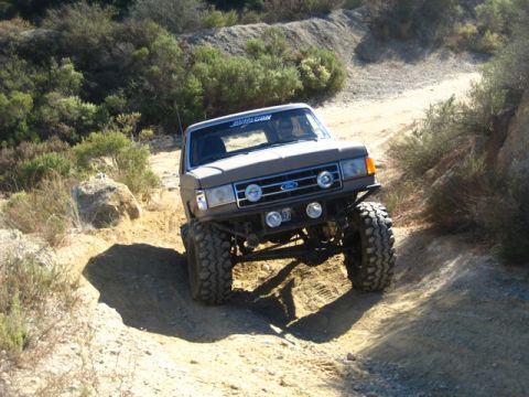1989 Ford Bronco - Modified Ford Bronco navigates a steep, dusty off-road path with large tires.