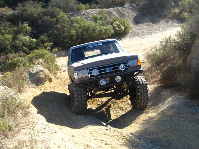 Lifted gray Ford SUV flexing through a dirt rut on a brushy hillside trail