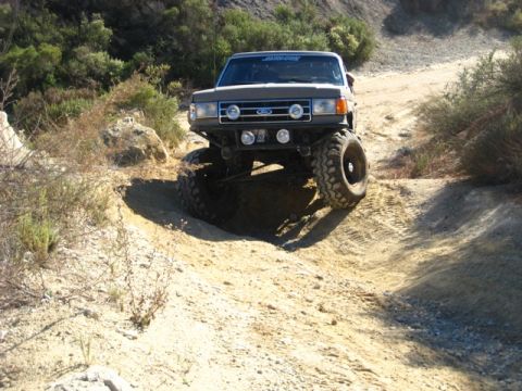 1989 Ford Bronco - This heavily modified Ford Bronco navigates a challenging off-road trail, its impressive suspension and tire clearance.