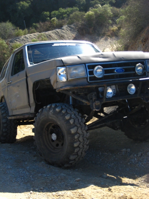 1989 Ford Bronco - Modified 1989 Ford Bronco with off-road tires and custom front bumper on a dirt road.