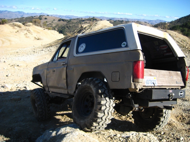 Tan Ford Bronco on black steel wheels and mud tires crawling rocks on a hillside trail