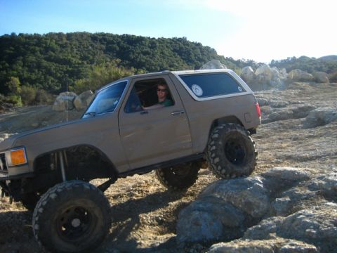 1989 Ford Bronco - This modified SUV navigates a challenging rocky path under a clear blue sky.