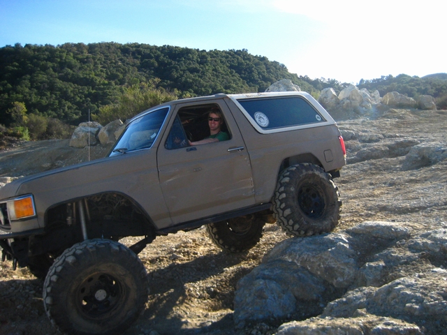 Tan two-door SUV lifted on mud tires crawling over rocks