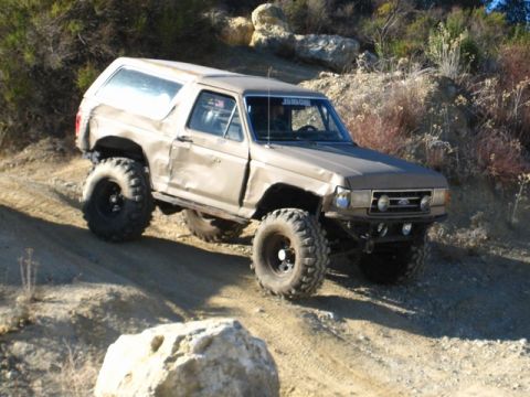 1989 Ford Bronco - This modified Ford Bronco navigates a rocky, off-road terrain under a clear sky.