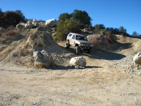 1989 Ford Bronco - A tan SUV navigates a challenging off-road course with large boulders and steep inclines.
