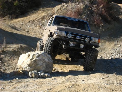 1989 Ford Bronco - This modified SUV, likely from the 1980s, tackles a challenging rocky terrain with its aggressive tires and lifted suspension.