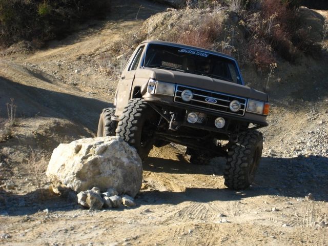 Tan lifted Ford Bronco climbing boulder with light bar and winch