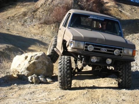 1989 Ford Bronco - A lifted 1989 Ford Bronco navigates a rocky obstacle on an off-road trail.