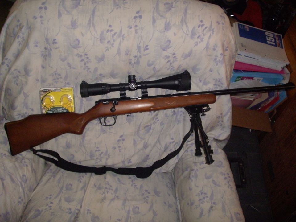Wood-stock bolt-action rifle with scope and bipod on a floral chair