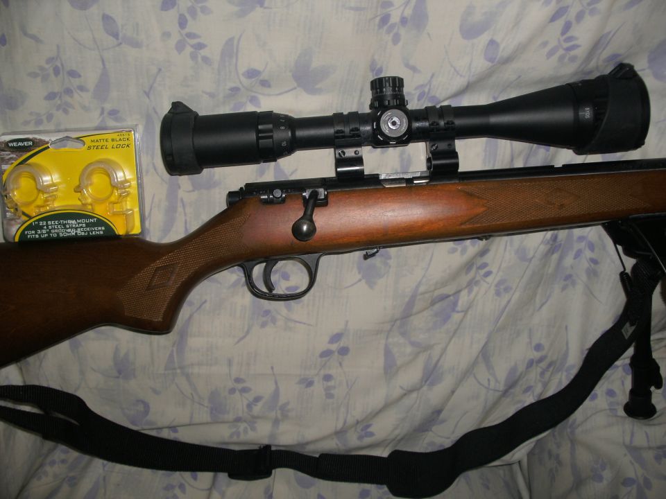 Bolt-action rifle with scope and Weaver mount package on a bed