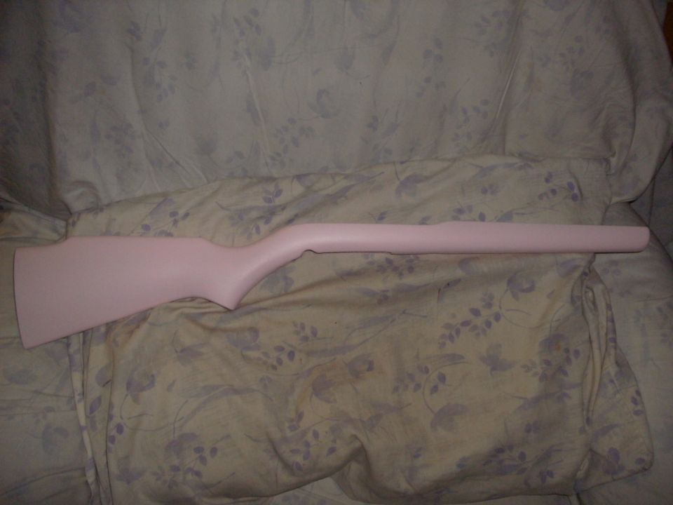 Pink-finished wooden rifle stock on a floral bedspread