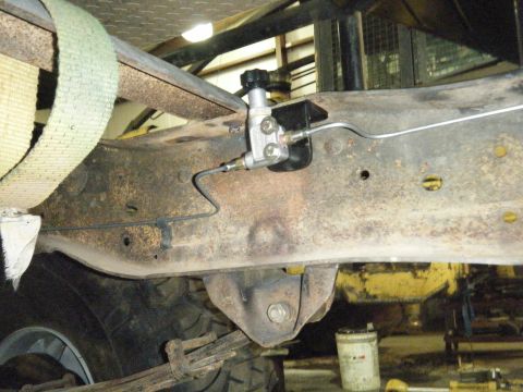 1978 Ford Bronco - Close-up view of a brake line valve assembly mounted to a heavily rusted vehicle frame, with a tire and leaf spring visible below.