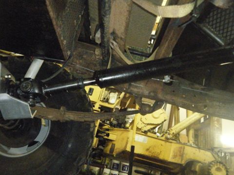 1978 Ford Bronco - The photo shows the undercarriage of a vehicle, including the driveshaft and leaf springs, with a yellow piece of equipment visible behind…