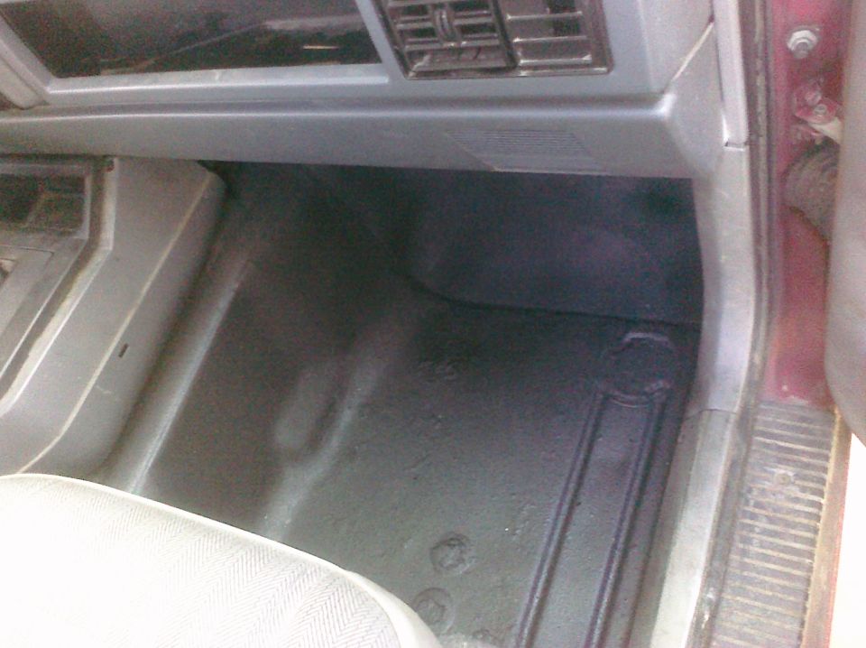 Vehicle interior showing floor, lower dashboard, and part of a seat. Water stains visible on the floor