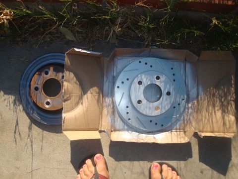 1995 Ford Taurus - A new slotted and drilled brake rotor is shown next to a rusty old rotor, likely for a vehicle brake replacement.