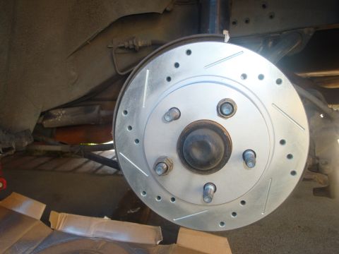 1995 Ford Taurus - Close-up of a new perforated and slotted brake rotor installed on a vehicle.
