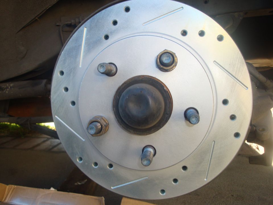 Close-up of a drilled and slotted brake rotor with lug nuts visible