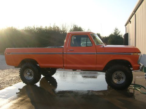 1975 Ford F-250 - Side view of a lifted orange pickup truck with large tires, parked on a wet surface.
