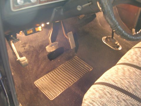 1975 Ford F-250 - The floor of the truck shows the clutch, brake, and gas pedals, along with a ribbed floor mat.