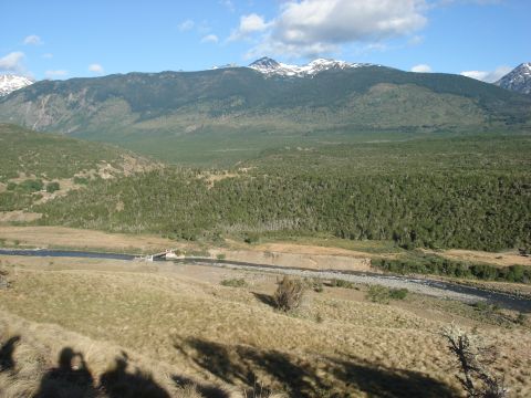 1986 Ford Bronco - A scenic view of a river winding through a valley, with dense forests and snow-capped mountains in the background.