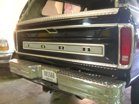 1975 Ford F-250 - Rear of a black Ford F-Series truck, showing the tailgate and chrome bumper. A white truck is visible to the left.