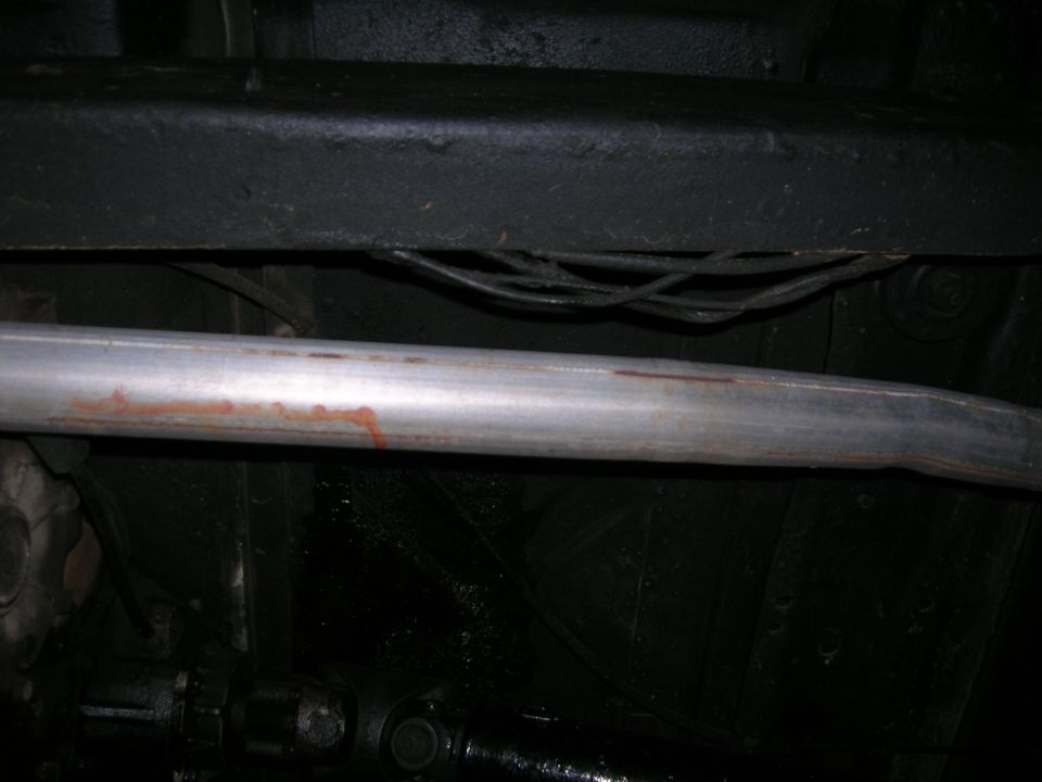 Underside of a vehicle showing an exhaust pipe with rust stains and part of the driveshaft