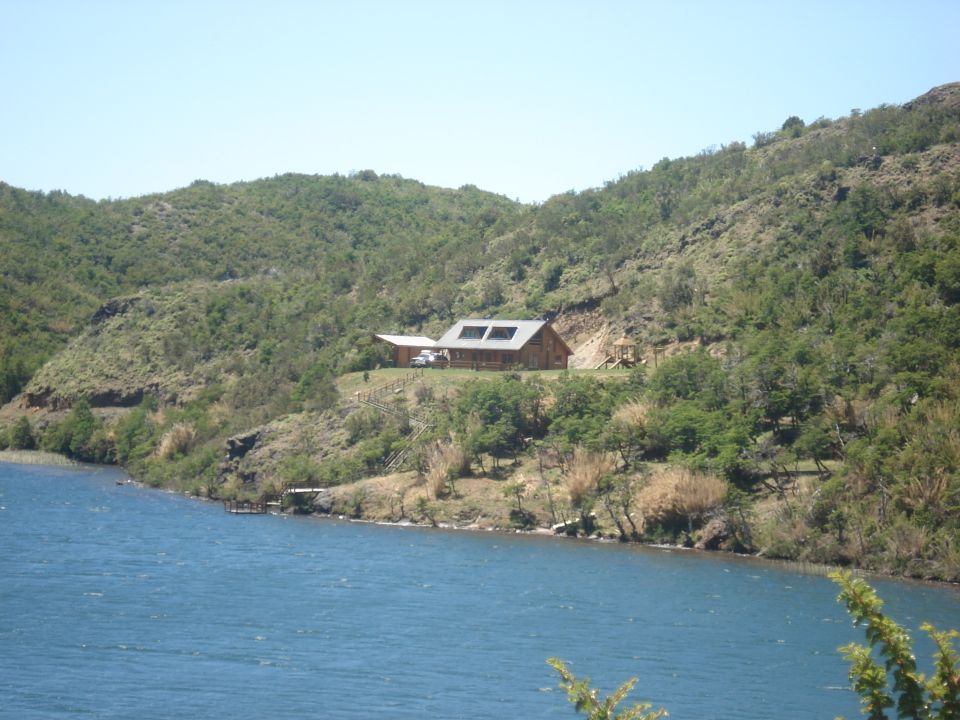 White SUV parked near a wooden house on a hillside overlooking a lake