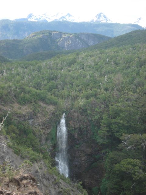 1986 Ford Bronco - A tall waterfall plunges into a valley, framed by lush trees and distant snowy peaks.