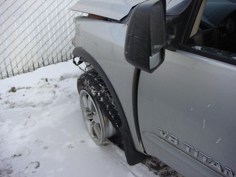 Silver Nissan V8 Titan pickup with crash-damaged front fender and mirror in snow