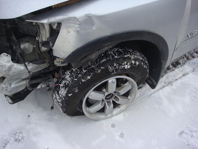 Silver SUV's damaged front fender and flat tire in the snow. The 'V8' badge is visible