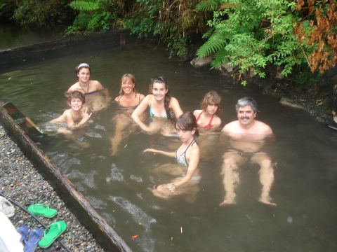 1986 Ford Bronco - A group of people enjoy a soak in a natural hot spring, with lush vegetation in the background.