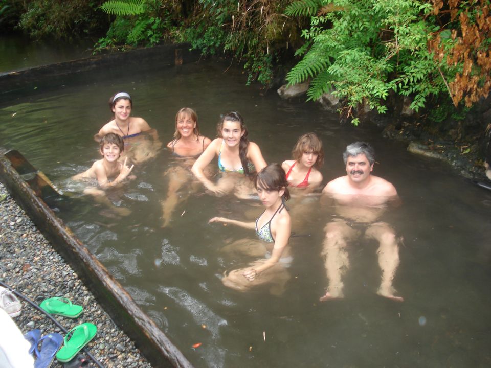group of people relaxing in a natural hot spring surrounded by greenery