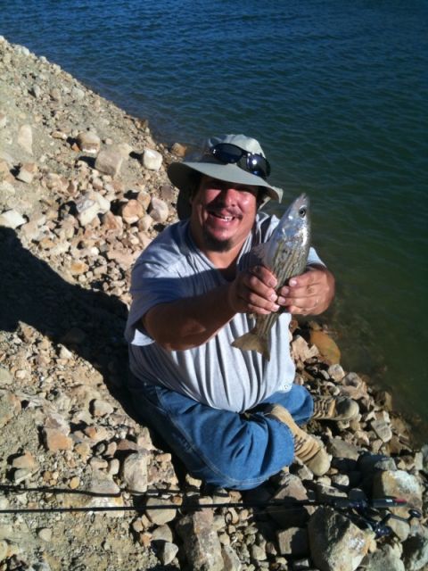 1968 Ford Mustang - A smiling man proudly displays a freshly caught striped fish while sitting by the rocky shore of a body of water.