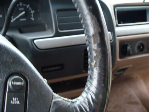 1993 Ford Bronco - The interior of a vehicle shows a worn steering wheel and the dashboard with gauges and air vents.