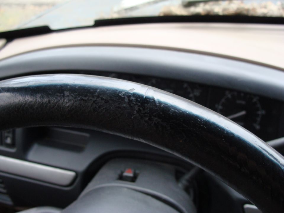 Black steering wheel with cracked leather, dashboard, and instrument cluster visible
